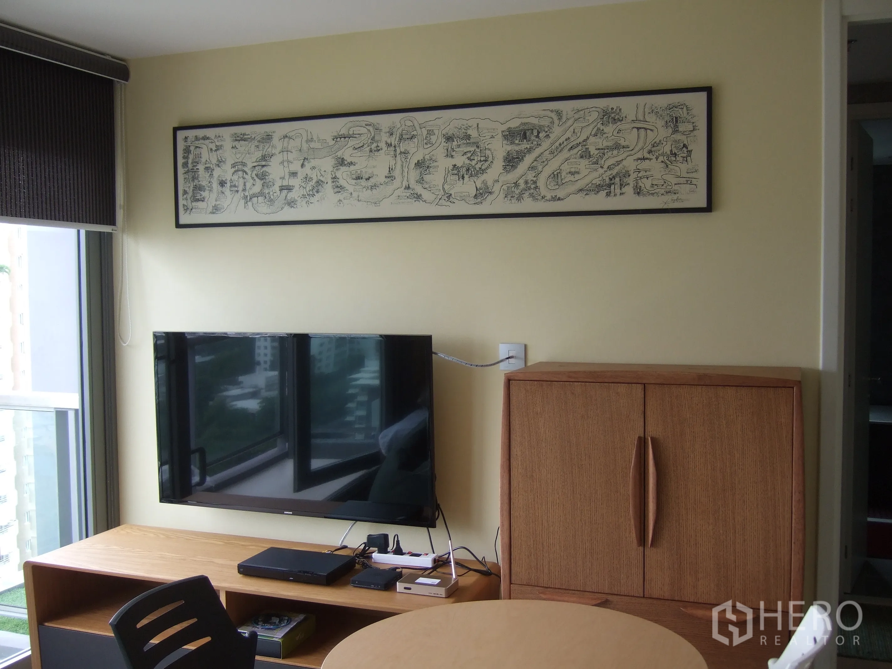 Condominium for rent or sale in Watthana, Bangkok - Cozy living area with wall-mounted TV, wooden cabinet, and large window.