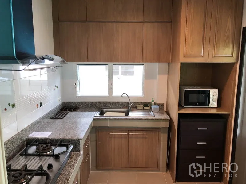 Detached House for rent or sale in Bang Kapi, Bangkok - Fitted kitchen with gas hob, range hood, granite countertops and wood cabinetry under a bright window.