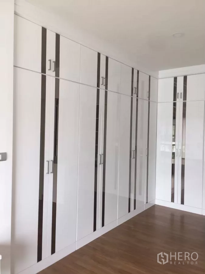 Detached House for rent in Samut Prakan - Wall of white built-in wardrobes offering generous storage in the bedroom.