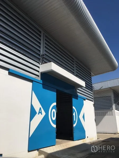 คลังสินค้า ให้เช่าในNong Chok, Bangkok - ด้านหน้าโกดังสมัยใหม่ ประตูบานเลื่อนสีน้ำเงิน พร้อมช่องลมระบายอากาศและหลังคาเมทัลชีทโค้ง ในเขตหนองจอก กรุงเทพฯ