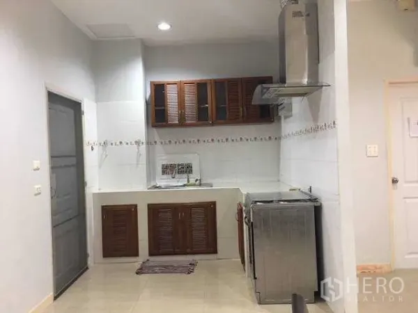 Home Office for rent in Wang Thonglang, Bangkok - Compact kitchen with wooden cabinets, white backsplash and stainless cooker hood in a Wang Thonglang, Bangkok home office.