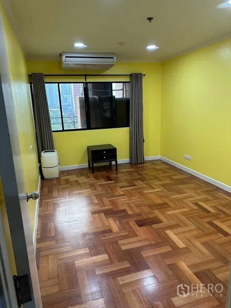 คอนโด ให้เช่าหรือขายในBangkok - ห้องนอนที่สอง ผนังสีเหลือง หน้าต่าง แอร์ และโต๊ะข้าง