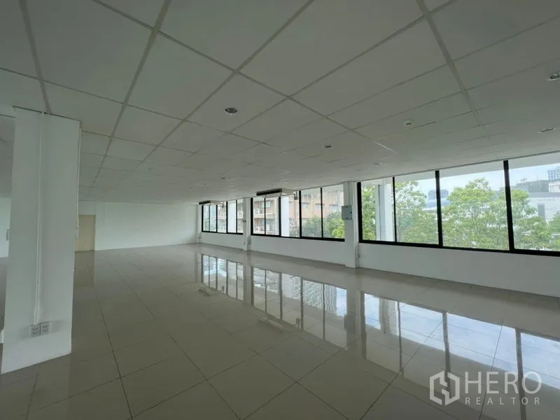 สำนักงาน ให้เช่า - สำนักงานกว้างโปร่ง หน้าต่างกรอบสีดำบานใหญ่ แสงธรรมชาติเต็มพื้นที่ มองเห็นเมืองและต้นไม้ พื้นกระเบื้องเงา