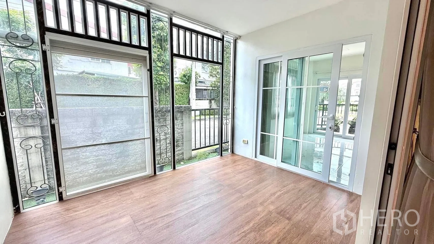 Detached House for rent or sale in Bueng Kum, Bangkok - Enclosed veranda with wood-look floor, glass panels and security grilles, linked by sliding doors.