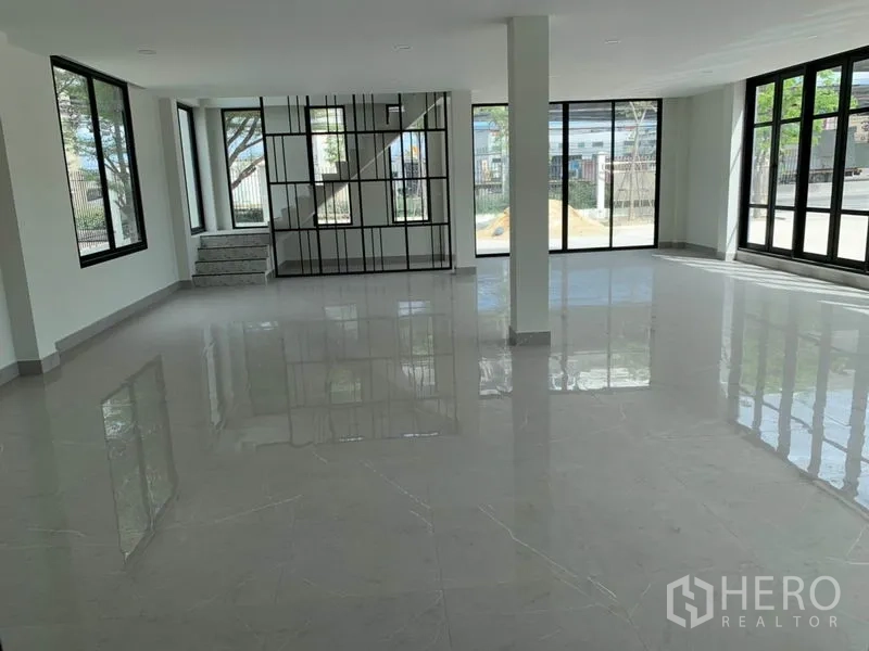 Warehouse for rent in Bang Phli, Samut Prakan - Ground-floor office area with a staircase and black metal partition, surrounded by wide windows for natural light.