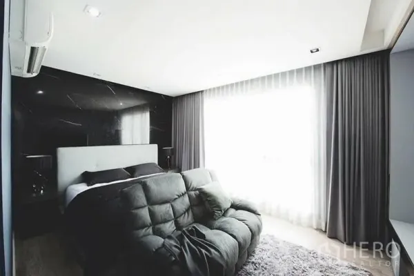 Townhouse for sale in Lak Si, Bangkok - Bright bedroom with sofa lounge, floor-to-ceiling curtains, and black feature wall.