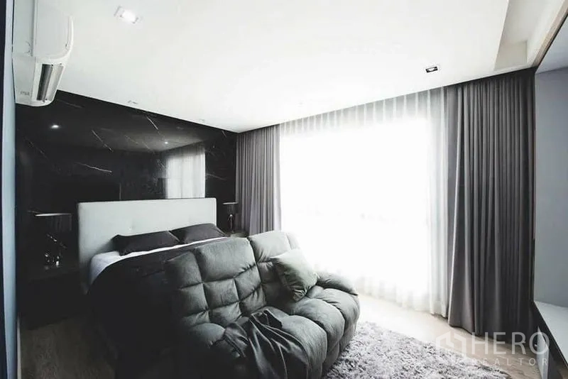 Townhouse for sale in Lak Si, Bangkok - Bright bedroom with sofa lounge, floor-to-ceiling curtains, and black feature wall.