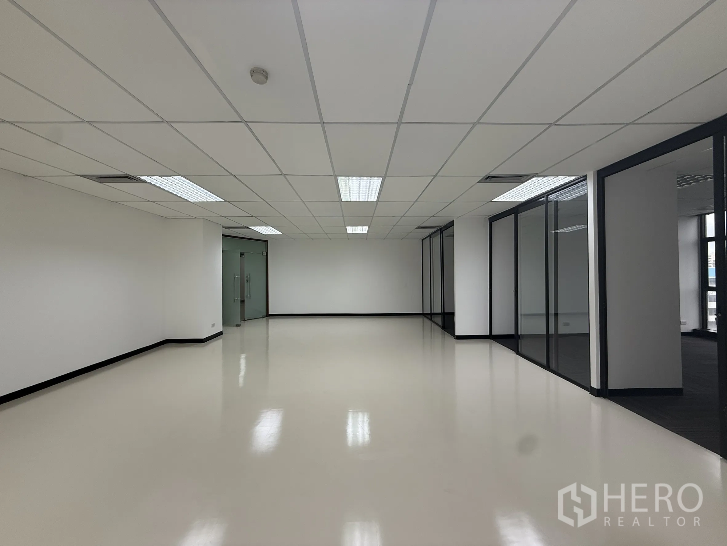 Office Space for rent - Bright collaboration or reception area with suspended ceiling lights, glass partitions, and a double glass-door entry.