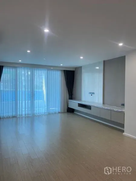 อพาร์ทเมนท์ ให้เช่าในWatthana, Bangkok - ห้องนั่งเล่นสว่าง โปร่งโล่งด้วยผนังกระจกเต็มบาน ผ้าม่านโปร่ง ไฟดาวน์ไลท์ และชั้นวางทีวีบิลท์อิน พื้นไม้โทนอ่อน