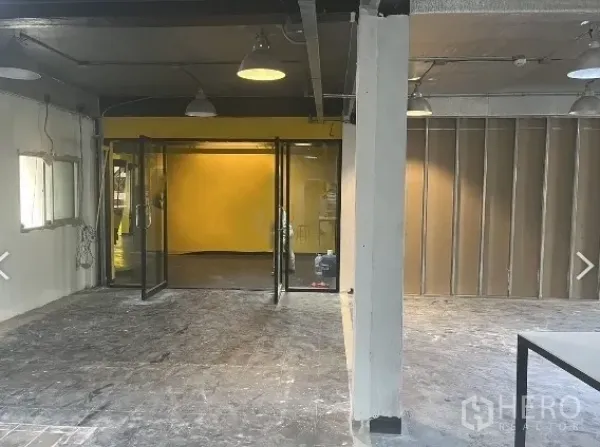 零售空间 出租在Pathum Wan, Bangkok - 帕吞旺区开放式零售室内，玻璃双开门与黄色特色墙，吊灯照明。