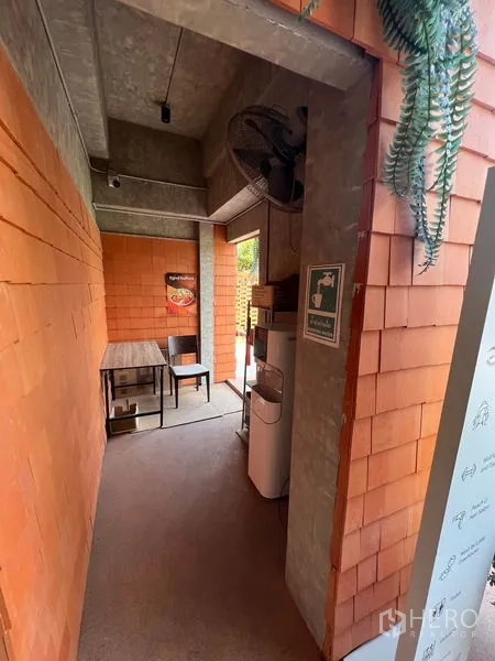 零售空间 出租在Watthana, Bangkok - 室内走道，清水混凝土天花、橙色瓷砖墙与小桌椅。