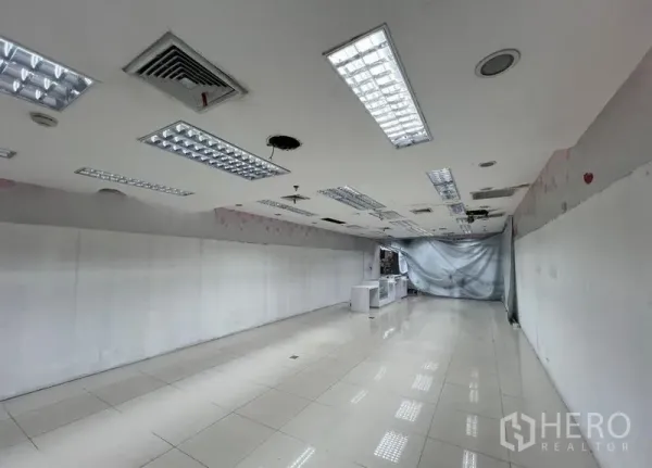 零售空间 出租 - 狭长型店铺室内，亮面地砖、空调出风口与网格灯具，待装修使用。