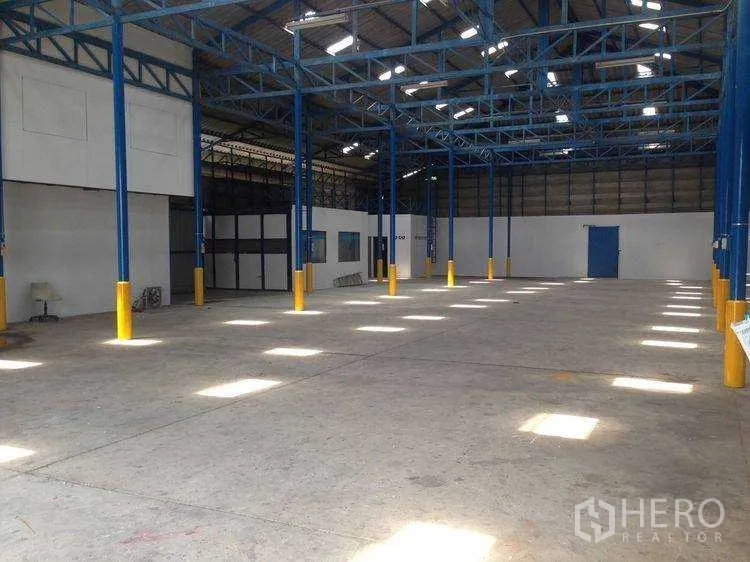 Warehouse for rent in Bang Kapi, Bangkok - Spacious warehouse interior with blue steel columns, skylights and concrete floor.