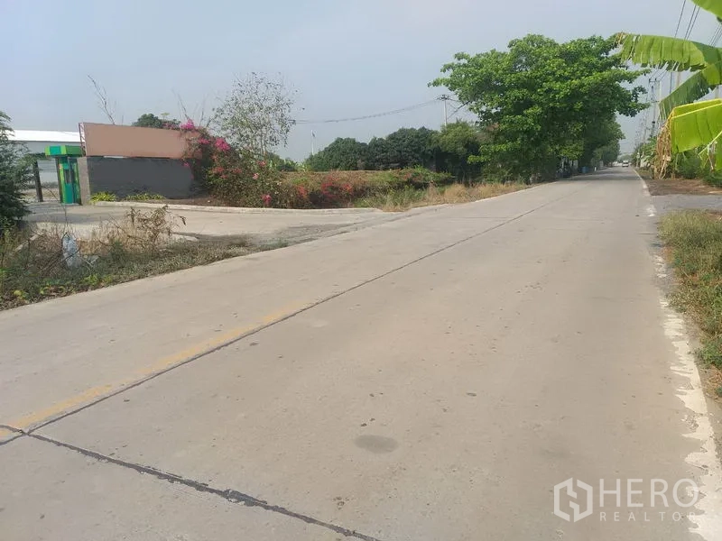Warehouse for rent in Pathum Thani - Quiet concrete access road near the property with surrounding greenery.