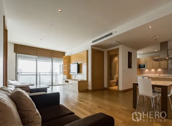 Condominium for rent in Watthana, Bangkok - Open-plan living area with wooden floors, built-in TV wall, and balcony city view next to the kitchen and dining area.