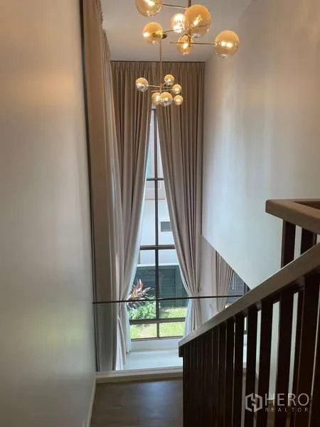 Detached House for rent in Bang Kapi, Bangkok - Staircase with high ceiling and designer chandelier facing tall window.