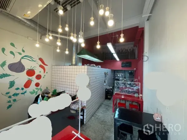 店屋 出租在Ratchathewi, Bangkok - 室内明亮，吊灯、白色瓷砖柜台、墙面蔬果壁画及靠近备餐区的座位。