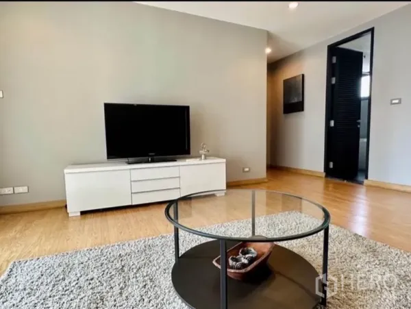 Condominium for rent in Watthana, Bangkok - Minimalist living room with TV console and round glass coffee table on a rug.