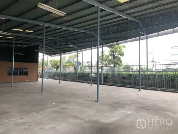 Warehouse for rent in Bang Phli, Samut Prakan - Covered loading area with open sides, metal fencing, and road frontage suitable for truck access.
