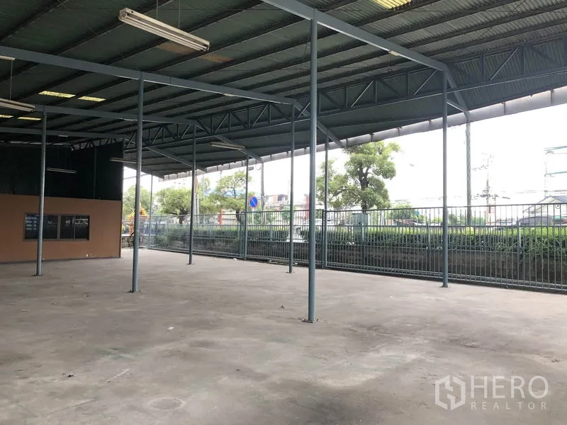 Warehouse for rent in Bang Phli, Samut Prakan - Covered loading area with open sides, metal fencing, and road frontage suitable for truck access.