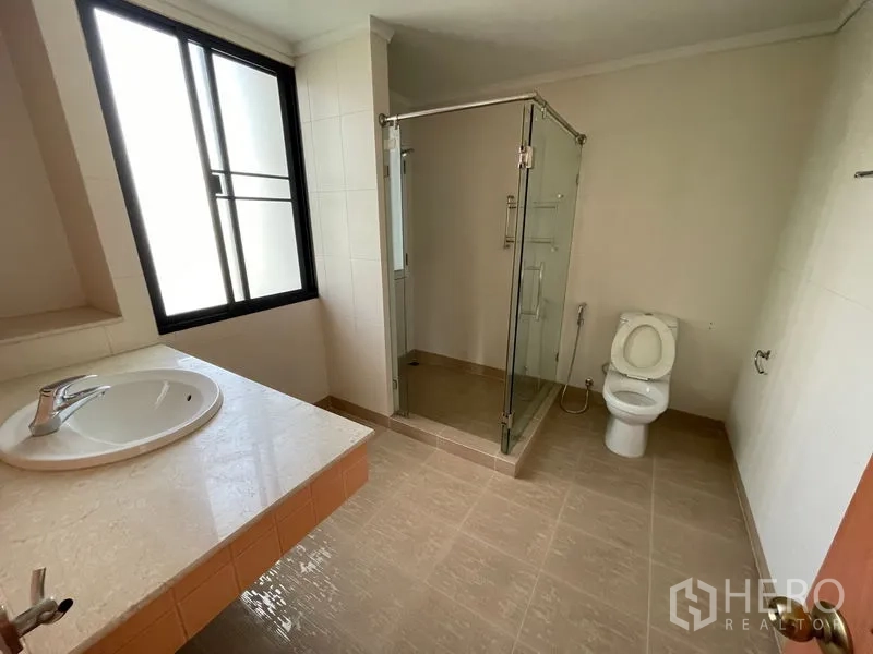 Condominium for rent in Watthana, Bangkok - Modern bathroom with glass-enclosed shower, vanity countertop and window.