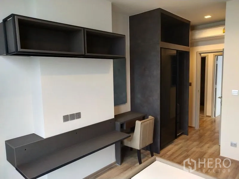 Condominium for rent in Chatuchak, Bangkok - Bedroom area with built-in desk, wall shelves, and a dark wardrobe over wood flooring.