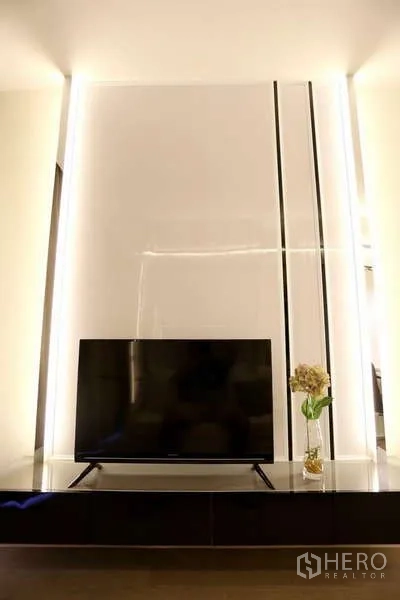 Condominium for rent in Watthana, Bangkok - Close-up of flat-screen TV on floating console against backlit glossy panel.