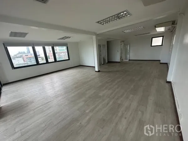 Office Space for rent in Sathon, Bangkok - Spacious office floor featuring wide windows overlooking the skyline, neutral walls, ceiling fluorescent lighting, structural columns, and access to a restroom and utility area.