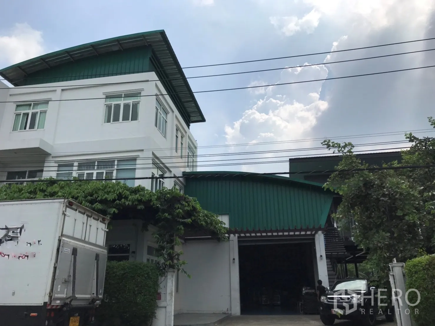 工厂 出售在Lam Luk Ka, Pathum Thani - 工厂正面，白色办公翼楼、外部楼梯、带藤蔓雨棚与卡车通道