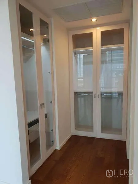 Condominium for rent in Sathon, Bangkok - Walk-in closet corridor with glass-door wardrobes and wood flooring.