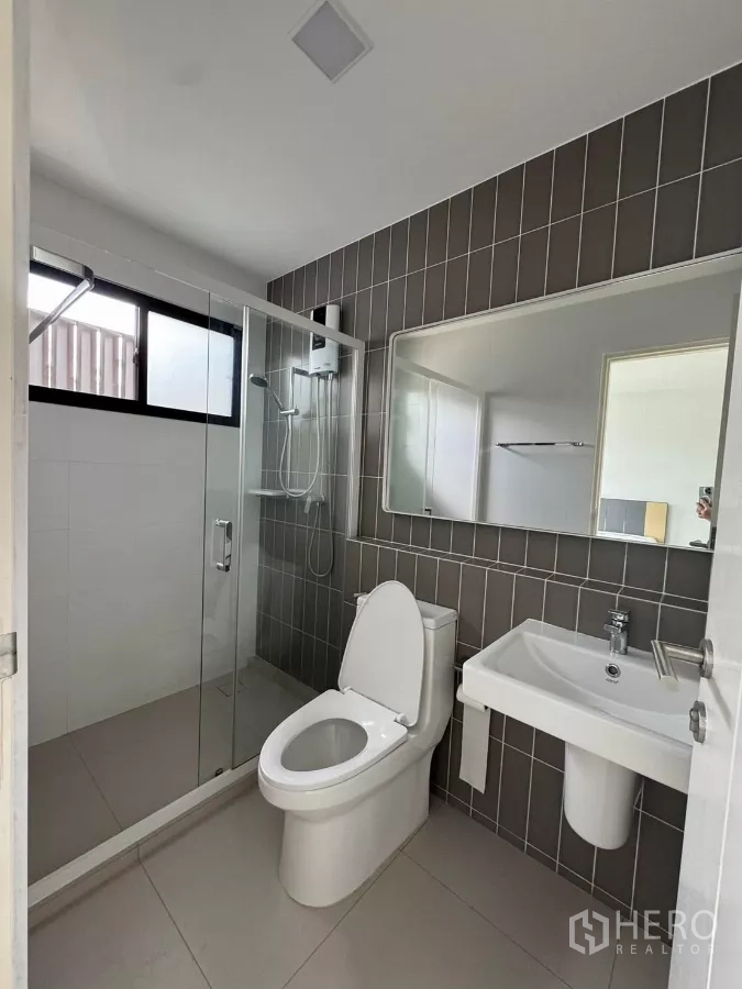 Townhouse for rent in Bang Phli, Samut Prakan - Second bathroom with shower enclosure, large mirror, and vertical tiles.