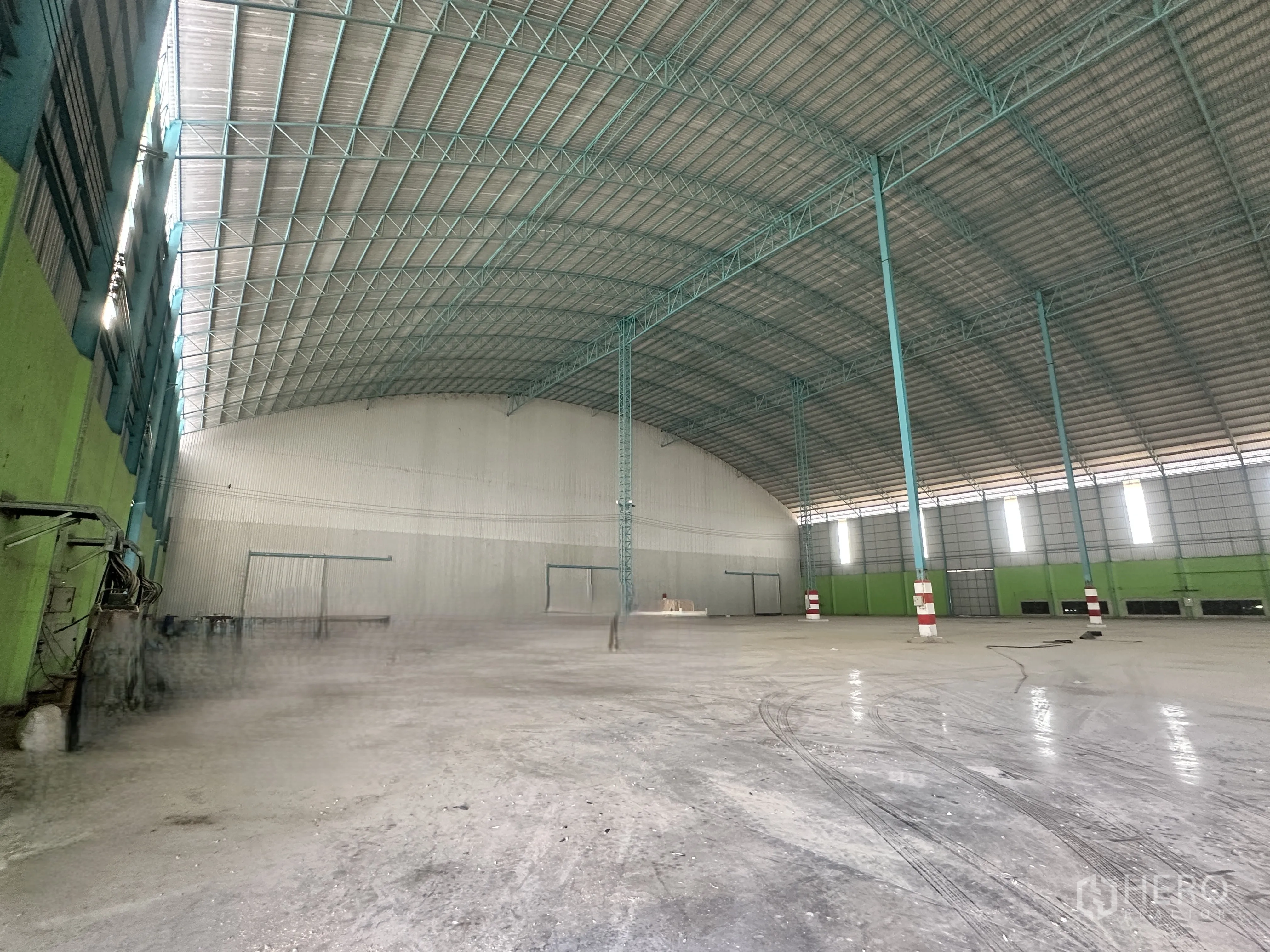 仓库 for rent in Sai Noi, Nonthaburi - 仓库内部视角：高拱形金属屋顶、开阔混凝土地面、钢柱与卷帘门。