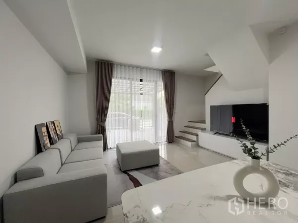 ทาวน์เฮาส์ ให้เช่าในBang Phli, Samut Prakan - โถงรับแขกแบบเปิดโล่ง พร้อมโซฟา ออตโตมัน ชุดวางทีวี และบันไดหันสู่หน้าบ้าน