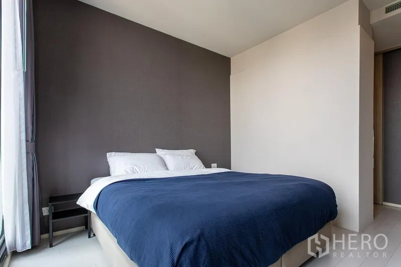 Condominium for rent in Pathum Wan, Bangkok - Cozy bedroom with large bed, dark accent wall and tall curtained windows in Bangkok condo