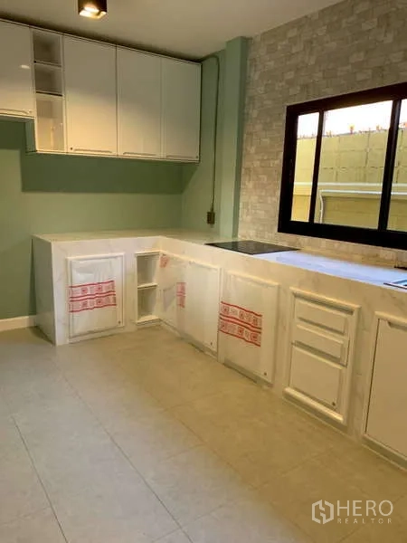 独立式住宅 出租或出售在Phra Khanong, Bangkok - 现代厨房，白色橱柜、石纹背景墙与窗边灶台。