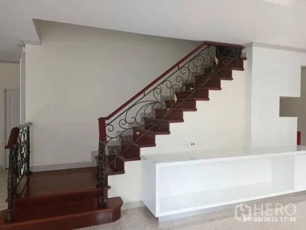 独立式住宅 出售在Prawet, Bangkok - 室内楼梯，红木踏步与锻铁栏杆，旁有白色柜台。