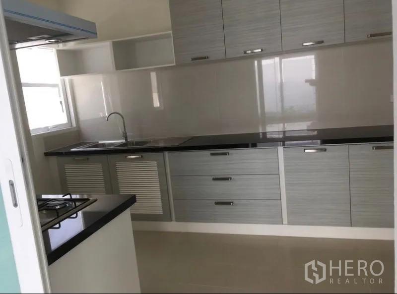 Detached House for rent or sale in Bang Na, Bangkok - Fitted kitchen with long black countertop, sink and ample storage cabinets.