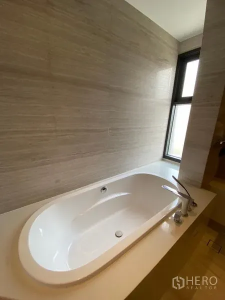 Detached House for rent in Huai Khwang, Bangkok - Bathroom featuring a built-in bathtub beneath a window with beige tiled wall.