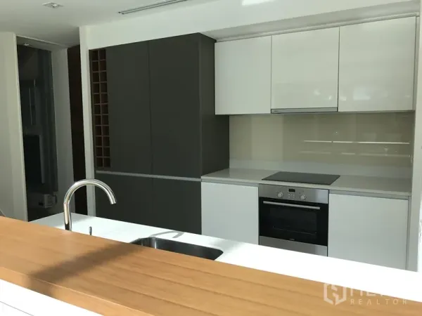 Condominium for rent in Khlong San, Bangkok - Modern kitchen with white and charcoal cabinets, built-in oven, electric cooktop, and sink island with wood counter.