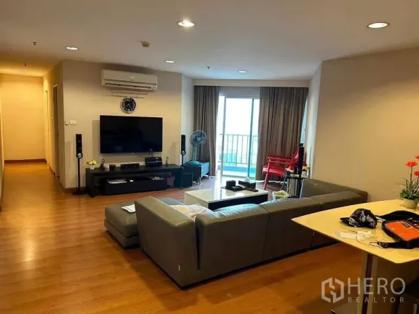 Condominium for sale in Huai Khwang, Bangkok - Spacious lounge with L-shaped sofa, TV console and sliding doors to a balcony.