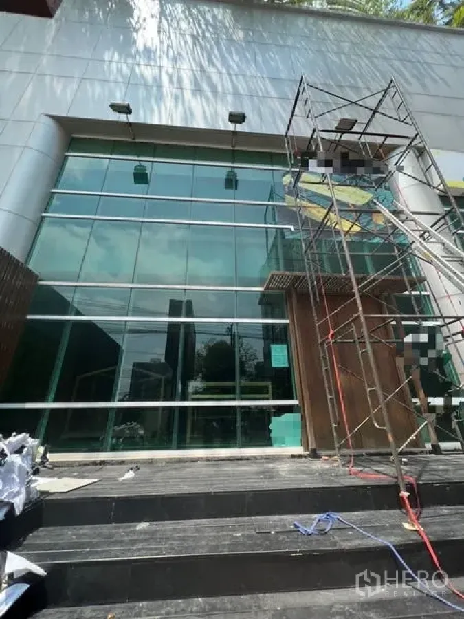 零售空间 出租在Khlong Toei, Bangkok - 现代零售建筑的双层通高玻璃门面，台阶与脚手架清晰可见。