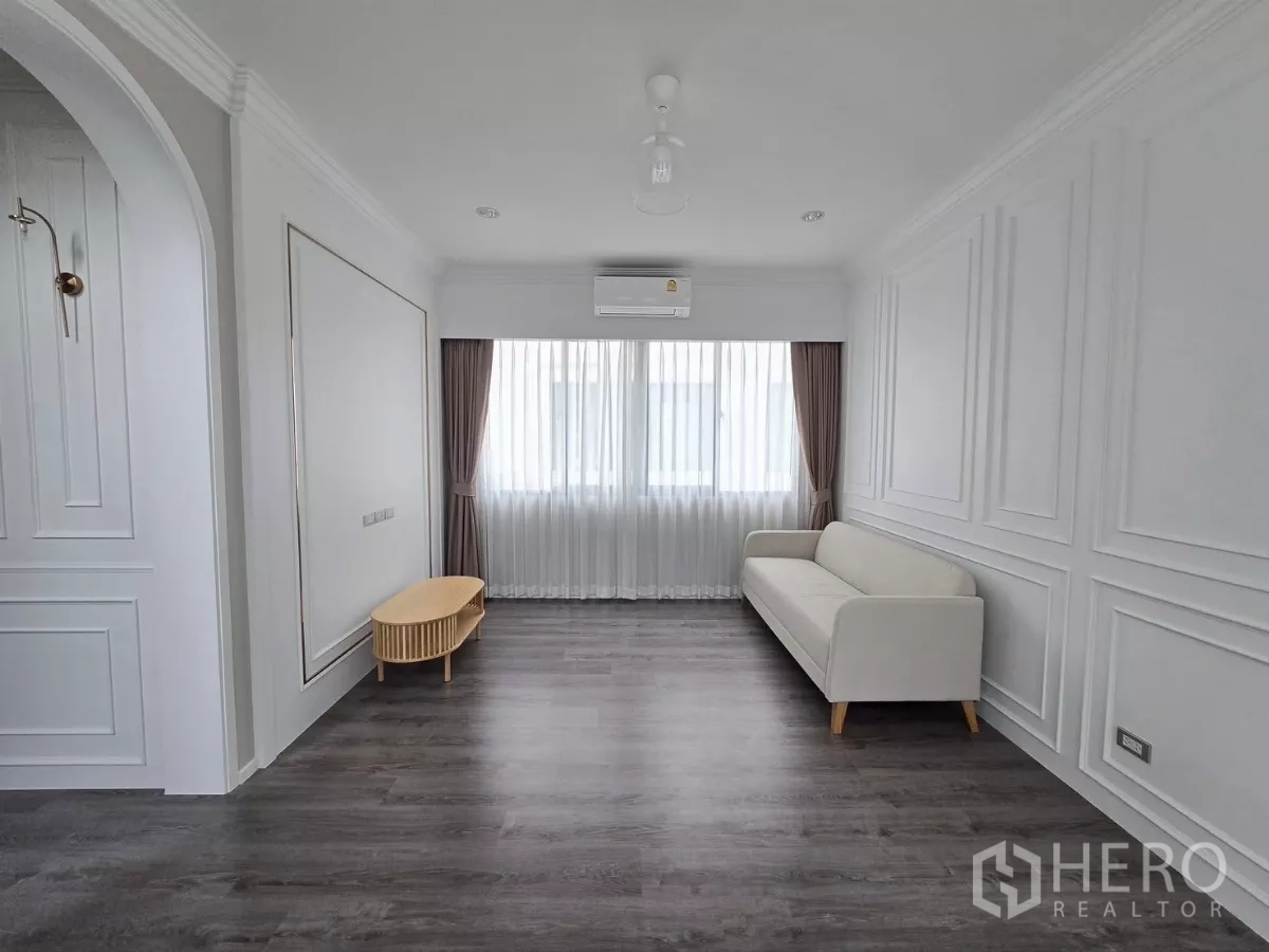 Detached House for rent in Prawet, Bangkok - Spacious family room with white sofa, wood floors and a large front window.