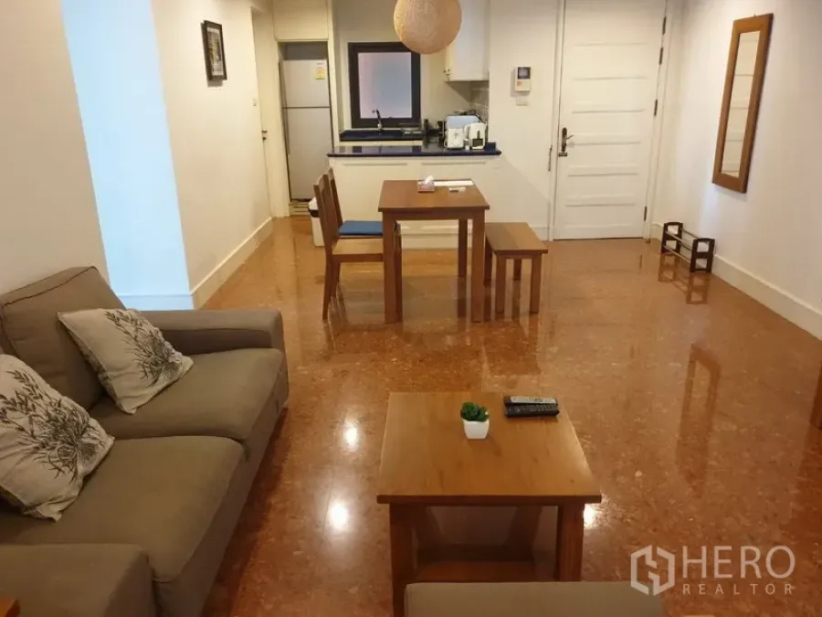 คอนโด ให้เช่าหรือขายในKhlong Toei, Bangkok - พื้นที่นั่งเล่นและรับประทานอาหารแบบโอเพ่นพร้อมโซฟา โต๊ะไม้ และครัวขนาดกะทัดรัดในคอนโดสมัยใหม่.