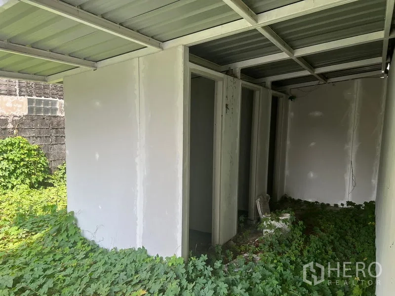 Warehouse for rent in Lat Krabang, Bangkok - Small outbuilding with multiple doorways showing unfinished utility rooms amid overgrowth.
