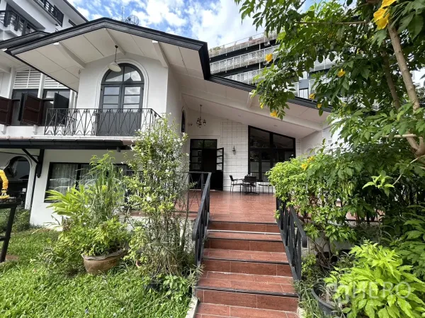 零售空间 出租在Bangkok - 白色低层商用建筑，拱形窗户，前花园与台阶通向有顶露台。