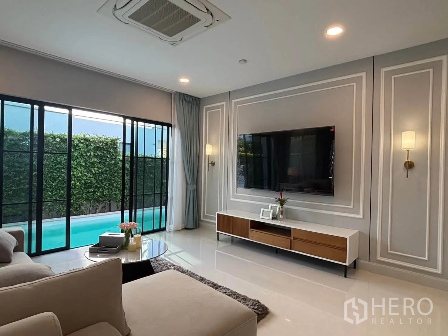 独栋房屋 for rent in Saphan Sung, Bangkok - 客厅电视墙，窗外可见泳池与绿篱花园。