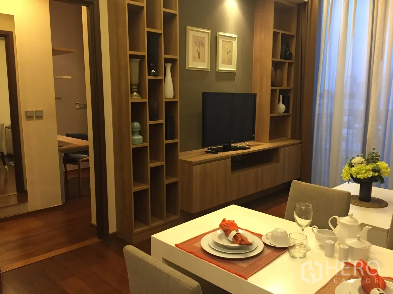 Condominium for rent or sale in Watthana, Bangkok - Warm-tone living and dining space with custom shelving, TV and table setting.