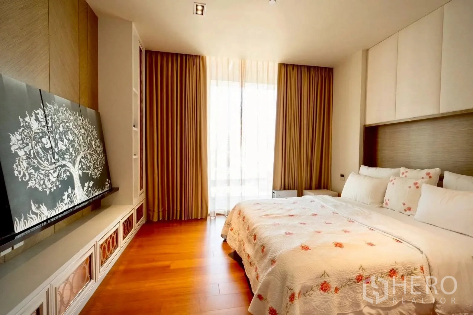 Condominium for sale in Sathon, Bangkok - Bedroom with floral bedspread, full-height curtains, and built-in storage.