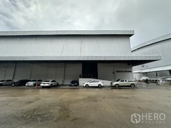 货栈 出租在Phra Nakhon Si Ayutthaya - 仓库正立面，深挑檐与停在装卸口前的车辆。