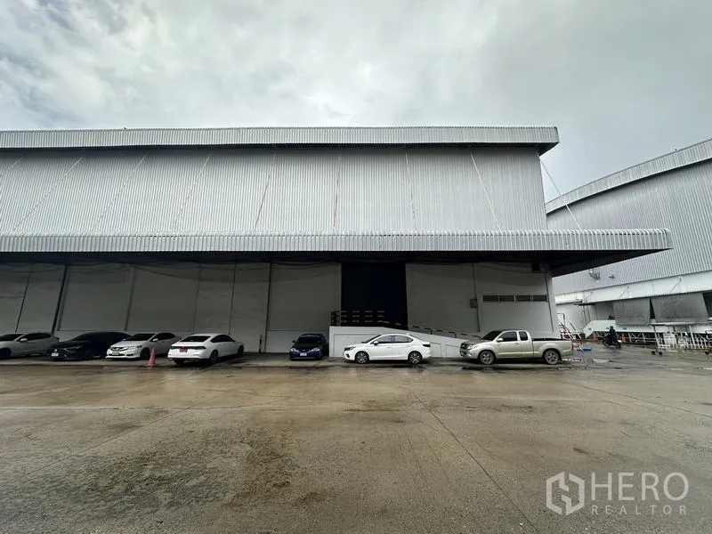 货栈 出租在Phra Nakhon Si Ayutthaya - 仓库正立面，深挑檐与停在装卸口前的车辆。